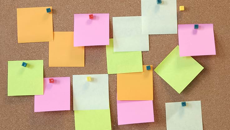 A corkboard with neon colored sticky notes pinned to a board.
