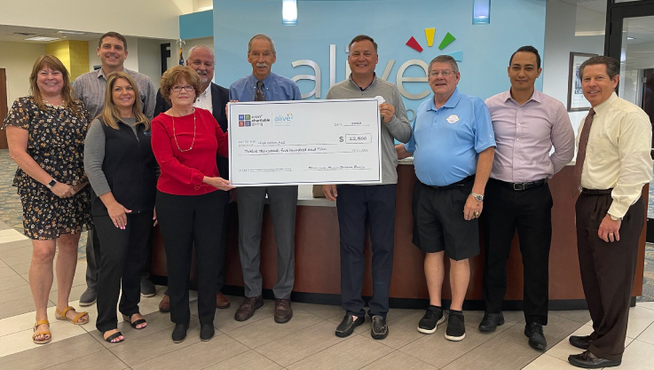 Ten individuals stand inside Alive Credit Union holding a large promotional check. 