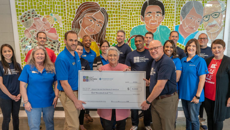 A group of adults stand holding two large checks.