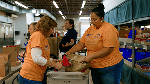 Two volunteers wearing orange shirts package an emergency box using tape. 