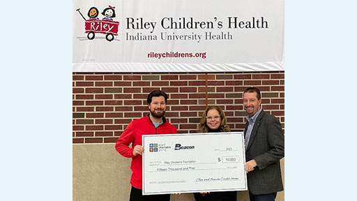 Three adults holding a big check in front of a brick wall.