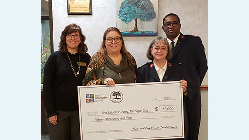 Group of four buisnesspeople holding a large check in an office.
