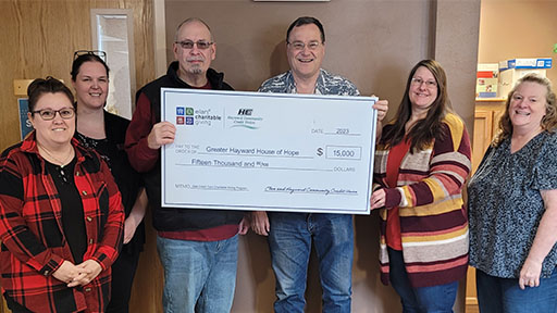 Group of 6 people holding a large check in front of a wood paneled wall.
