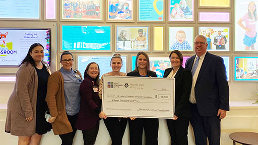 Group of seven people holding a  big check in front of a wall full of framed photographs.