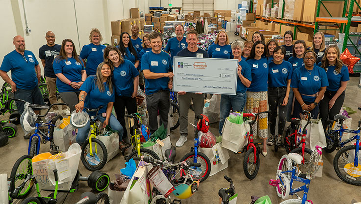 A group of volunteers stand behind children's bikes holding a large check. 