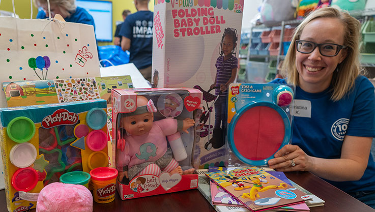 A volunteer poses next to a pile of gifts ready to be wrapped for a child's birthday.