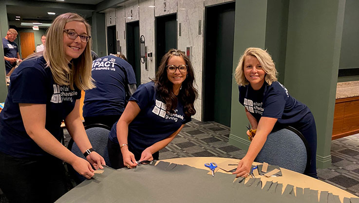 Three women stand behind a table holding large pieces of fleece for a blanket.