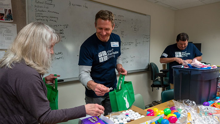 A group of volunteers stand around a table filling Easter baskets with candy, toys, and books. 