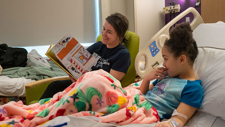 Elan employee reading to a child in hospital bed. 