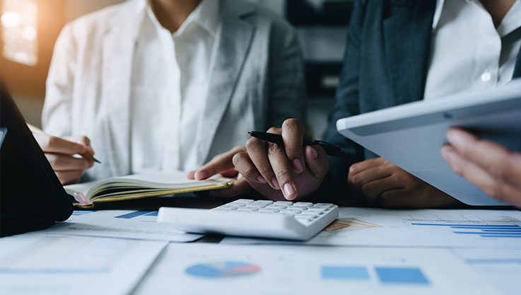 Two business people sit at a table. On the table are papers with graphs and charts. 